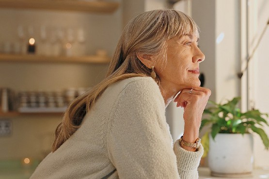 Senior woman smiling while looking out the window at home