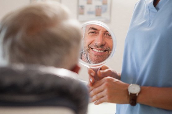 Man smiling at reflection in handheld mirror