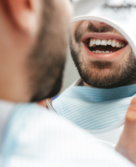Man smiling at reflection in handheld mirror