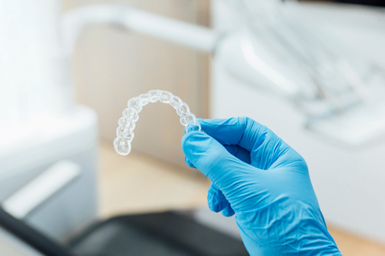 Dentist with blue glove holding clear aligner