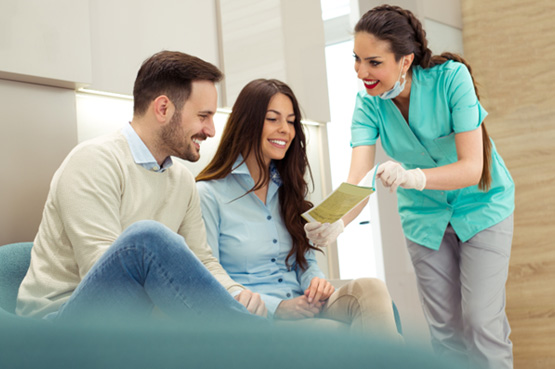 Smiling couple reviewing pamphlet with dental assistant