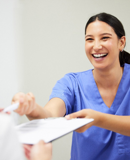 Smiling dental assistant handing patient forms